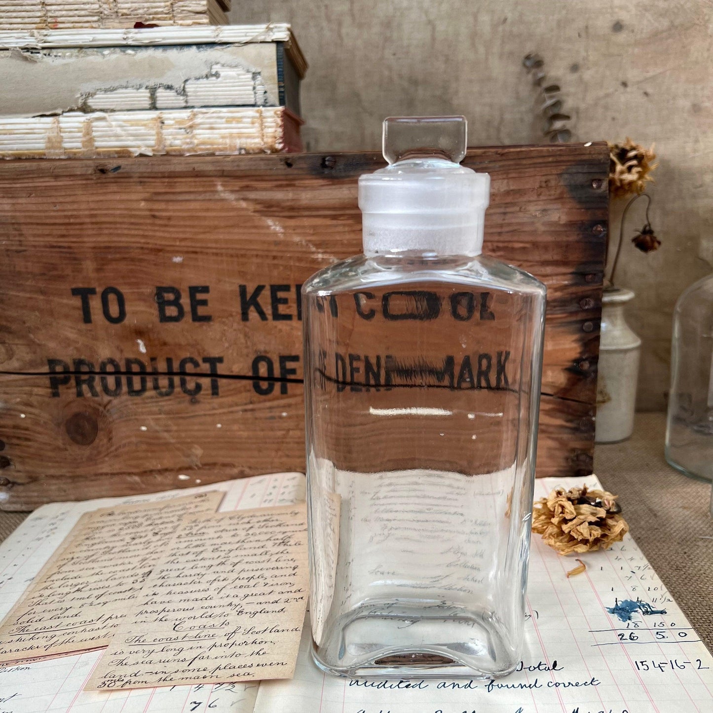 Clear vintage glass bottle with stopper on old handwritten papers and wooden crate background