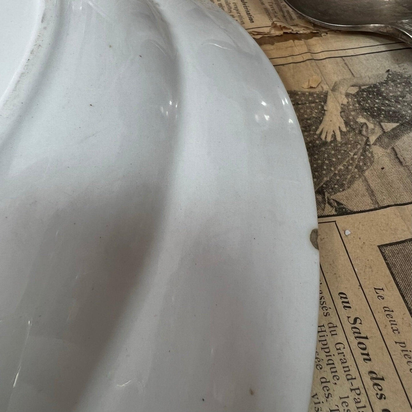 Close-up of a white ceramic object with chip on edge, resting on vintage newspaper with black-and-white photo