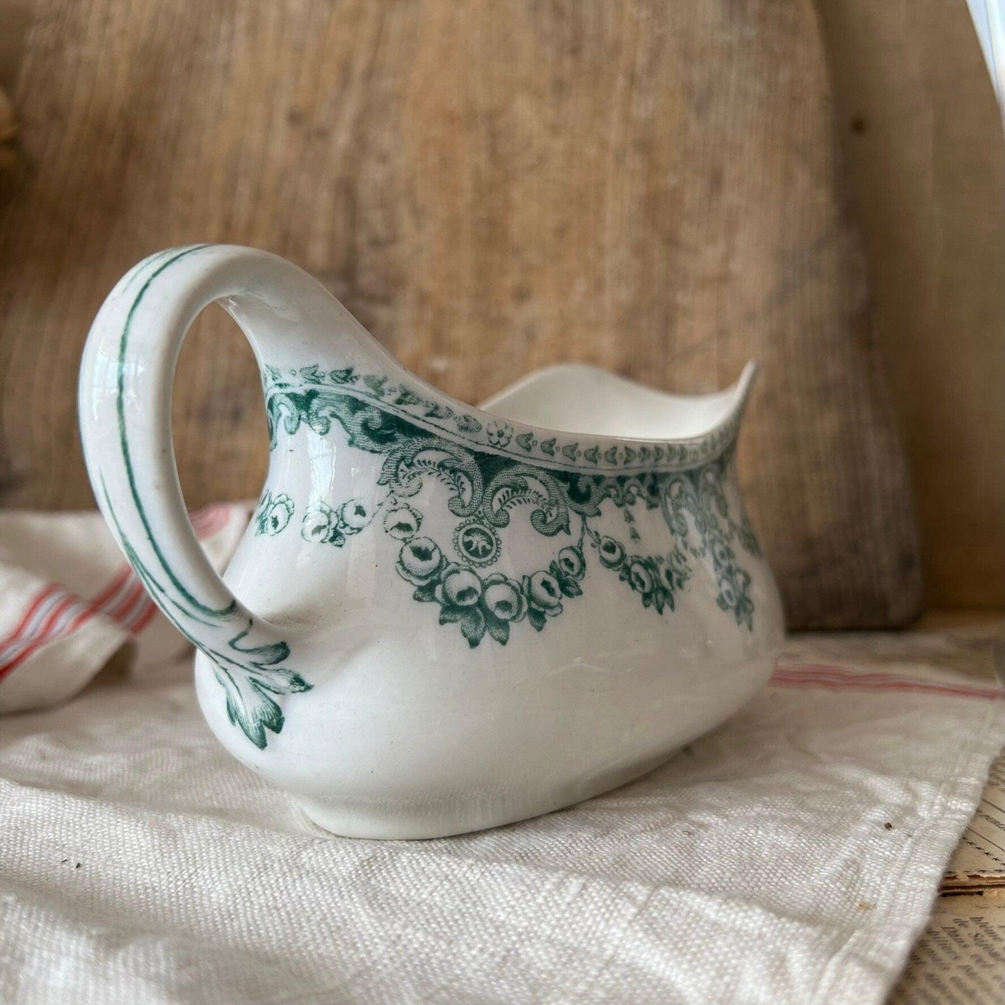 White ceramic gravy boat with green floral pattern on beige cloth and rustic wooden background