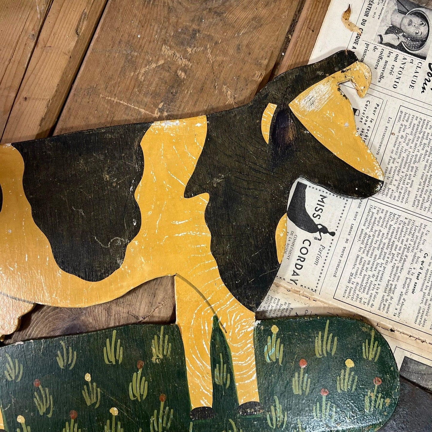 Vintage wooden cow cutout painted in yellow and black on rustic wooden floor with vintage newspaper