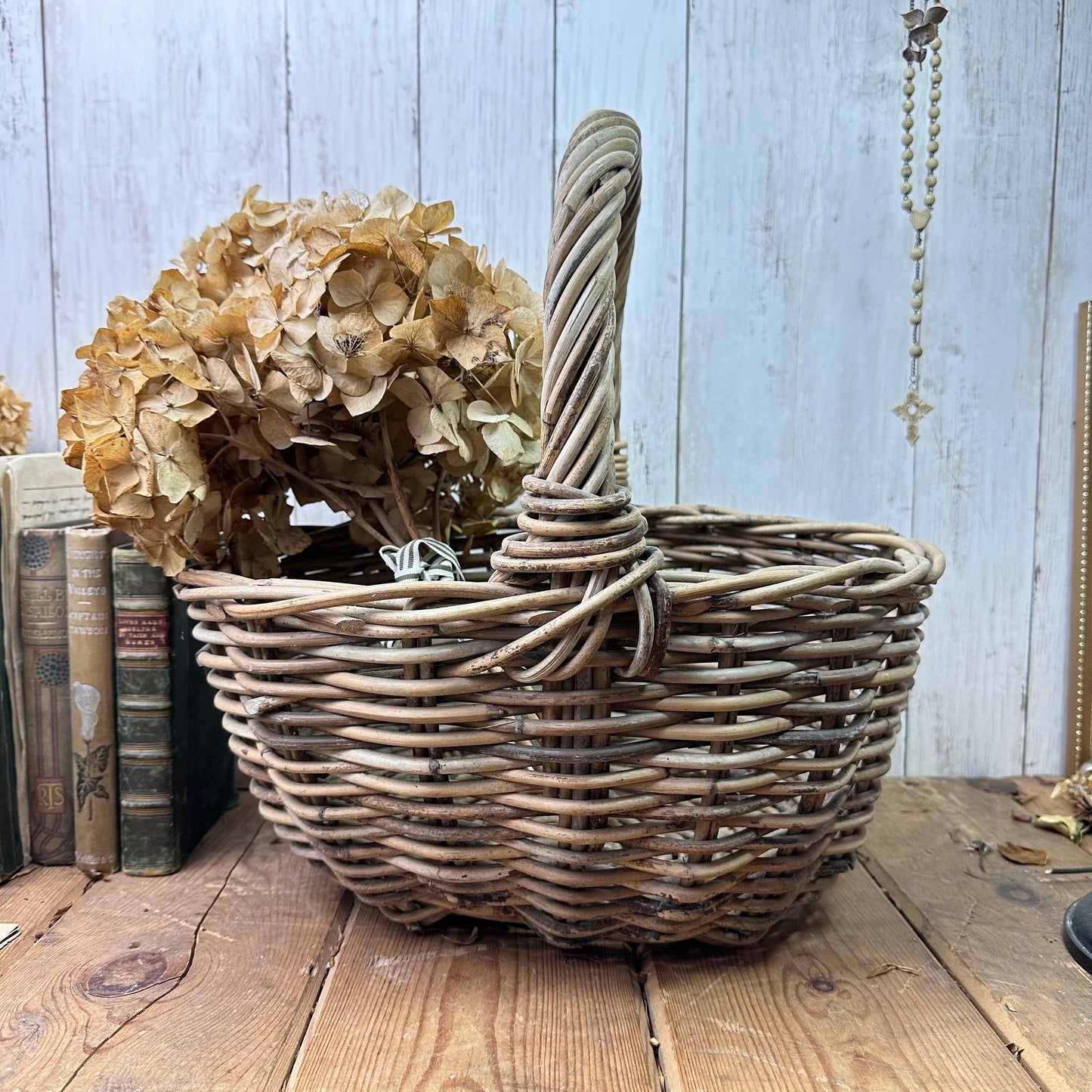 Rustic wicker basket with dried hydrangea flowers on wooden table against white wood panel background