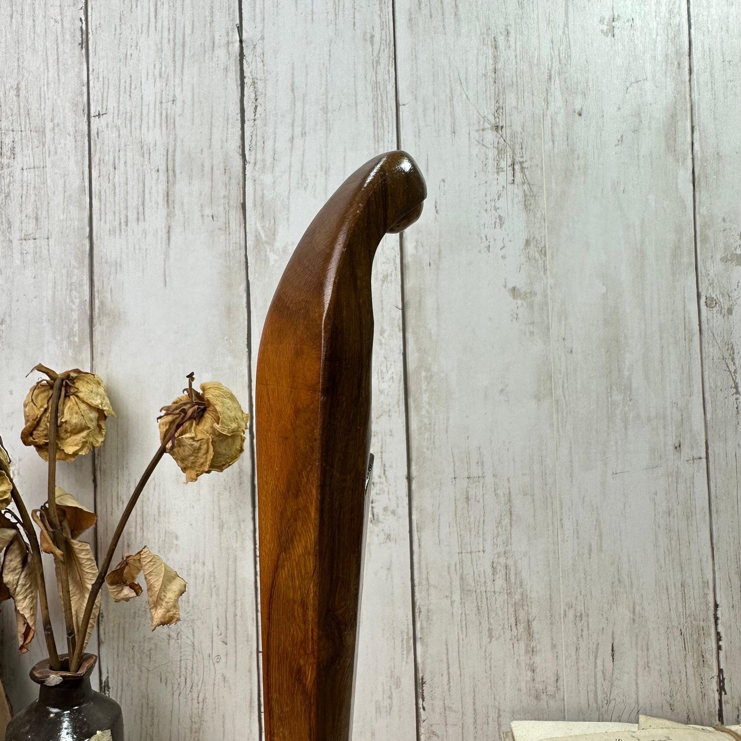 Polished wooden walking stick with curved handle beside dried flowers in rustic setting