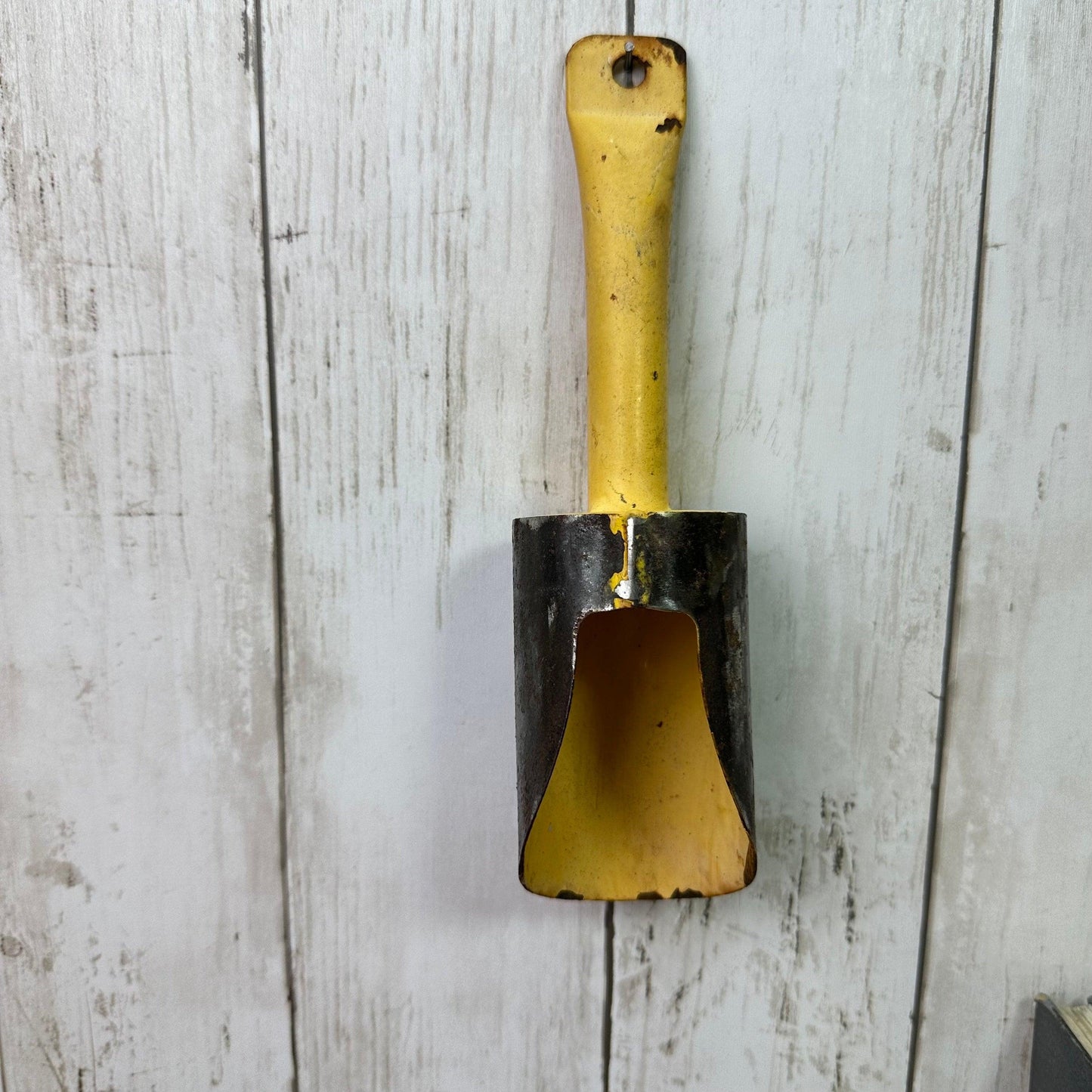 Vintage yellow and black metal scoop hanging on weathered white wooden wall