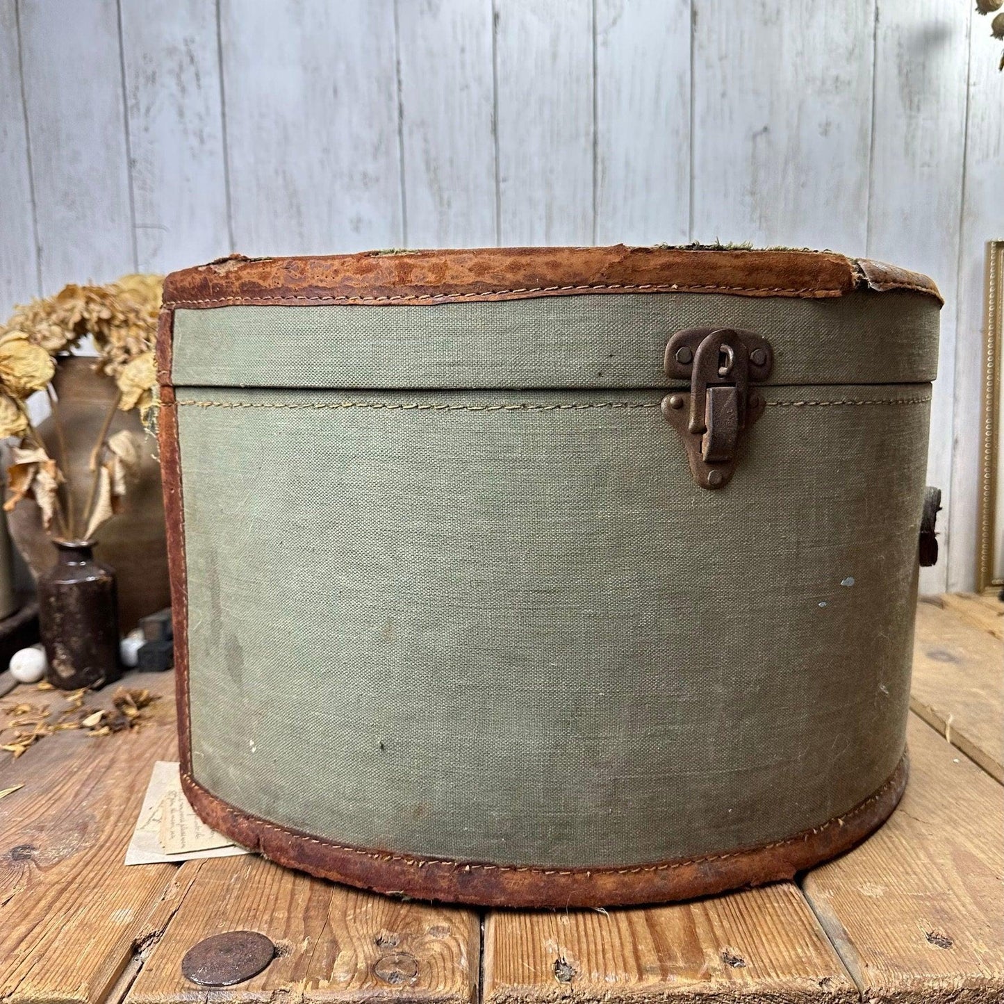Vintage oval green fabric hat box with brown trim and metal latch on wooden table