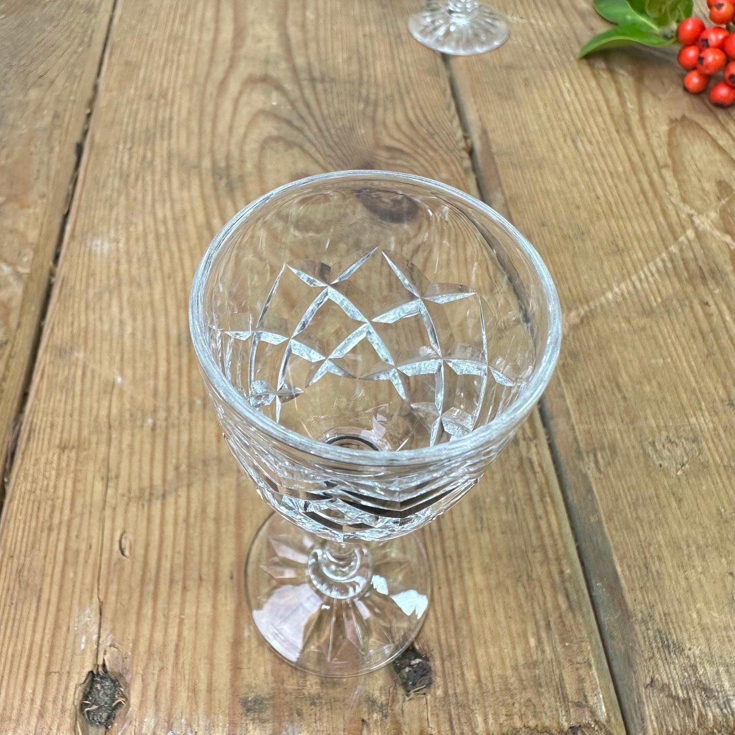 Close-up of empty crystal cut wine glass on rustic wooden table with holly berries nearby