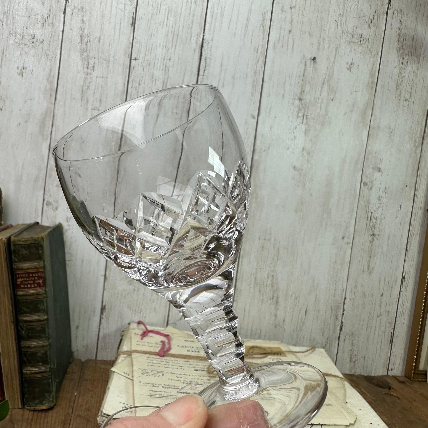 Hand holding a clear cut crystal wine glass with diamond patterns against a rustic wooden background and vintage books