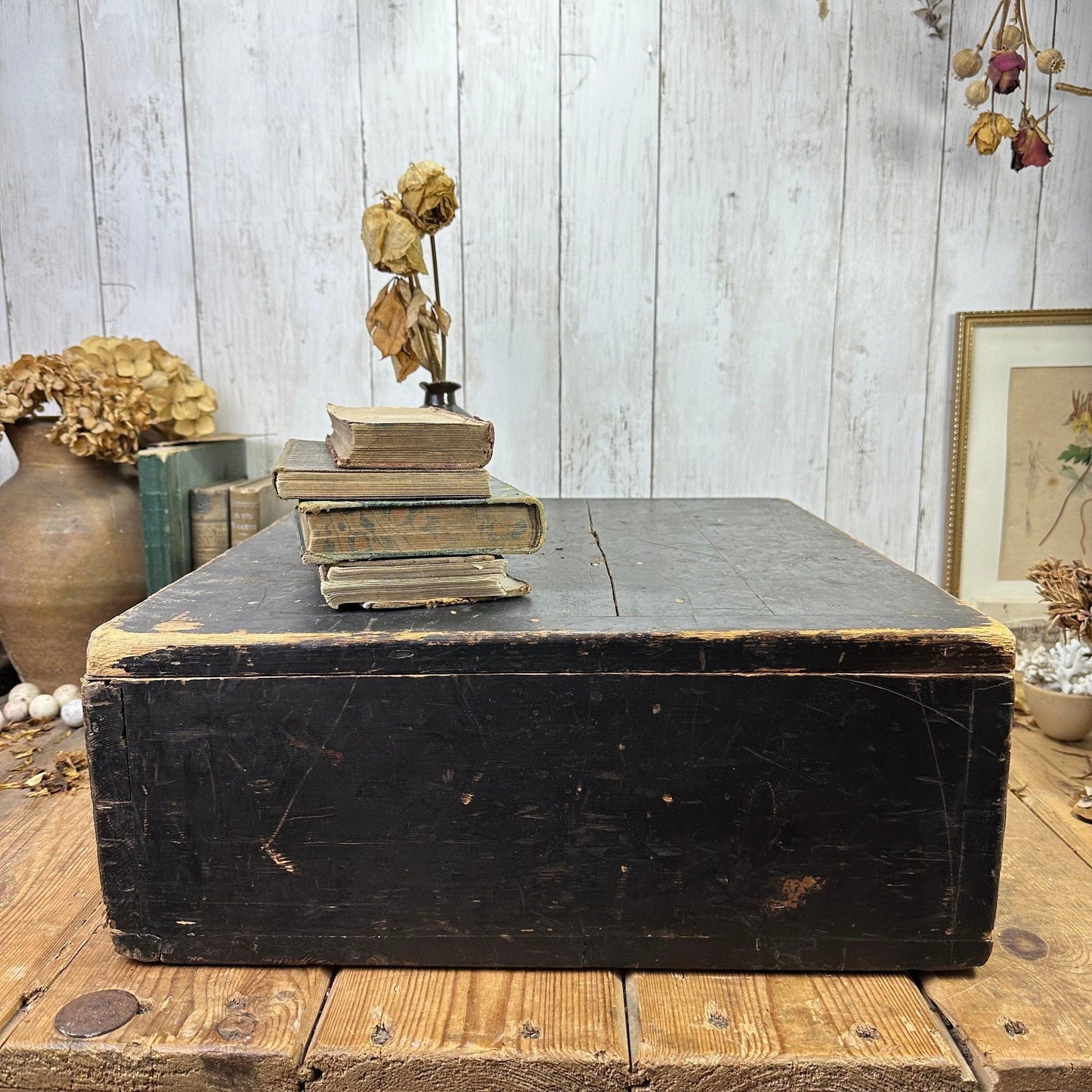 Vintage black wooden chest on rustic wood floor with old books and dried flowers in a cozy room