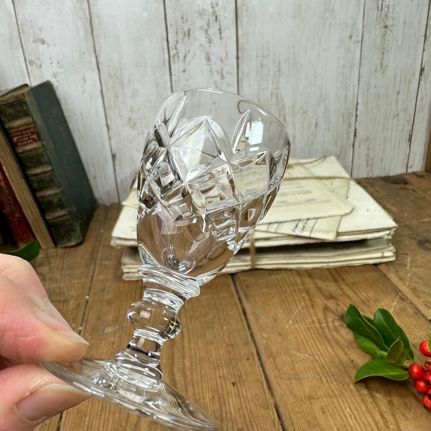 Hand holding a vintage cut crystal wine glass over a rustic wooden table with old books and tied letters
