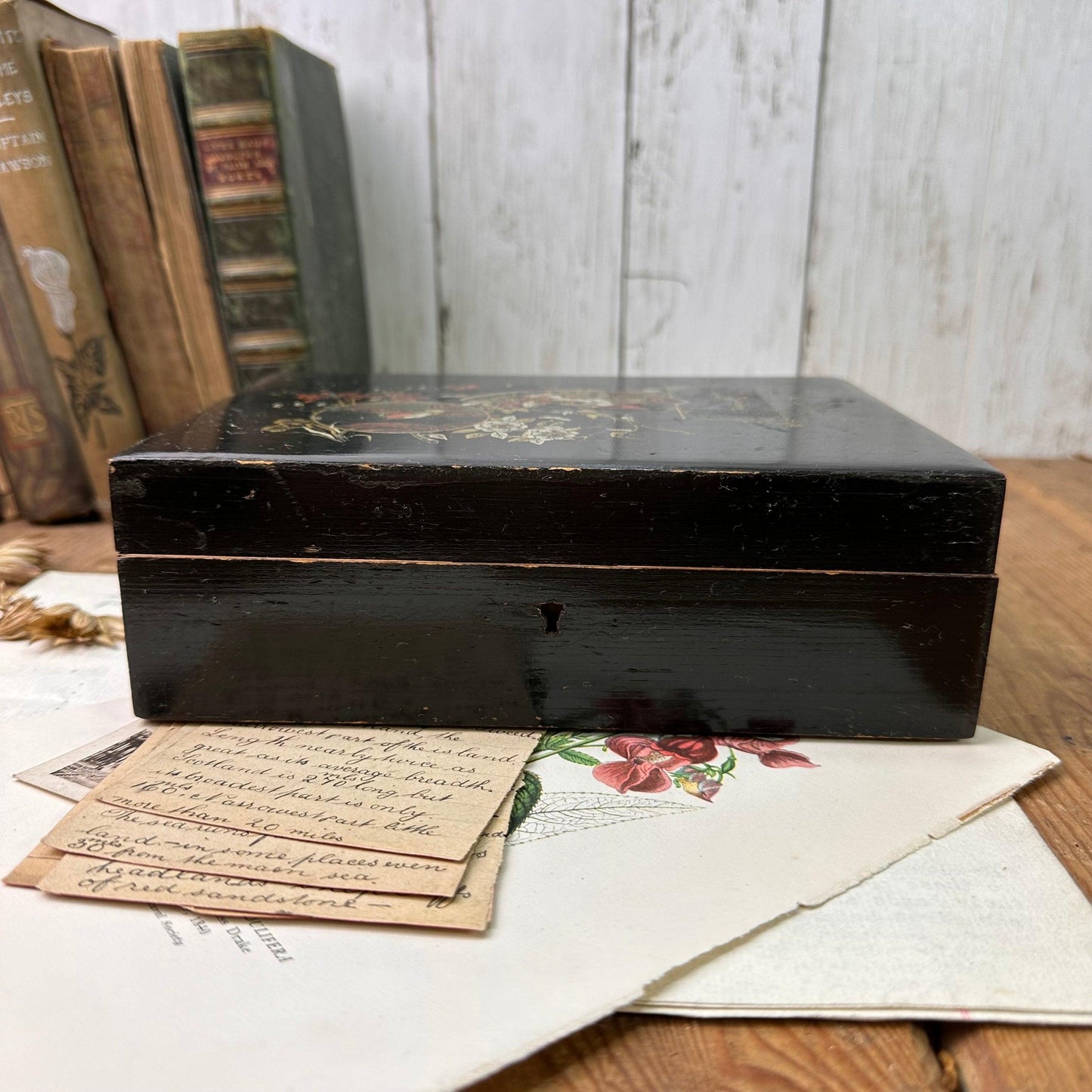 vintage black wooden box with floral design on top, resting on handwritten notes and botanical prints