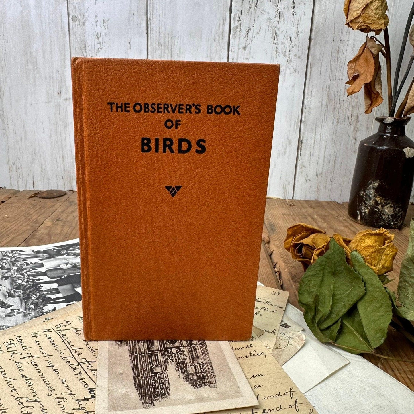 Vintage orange book titled The Observer's Book of Birds on wooden table with old letters and dried roses