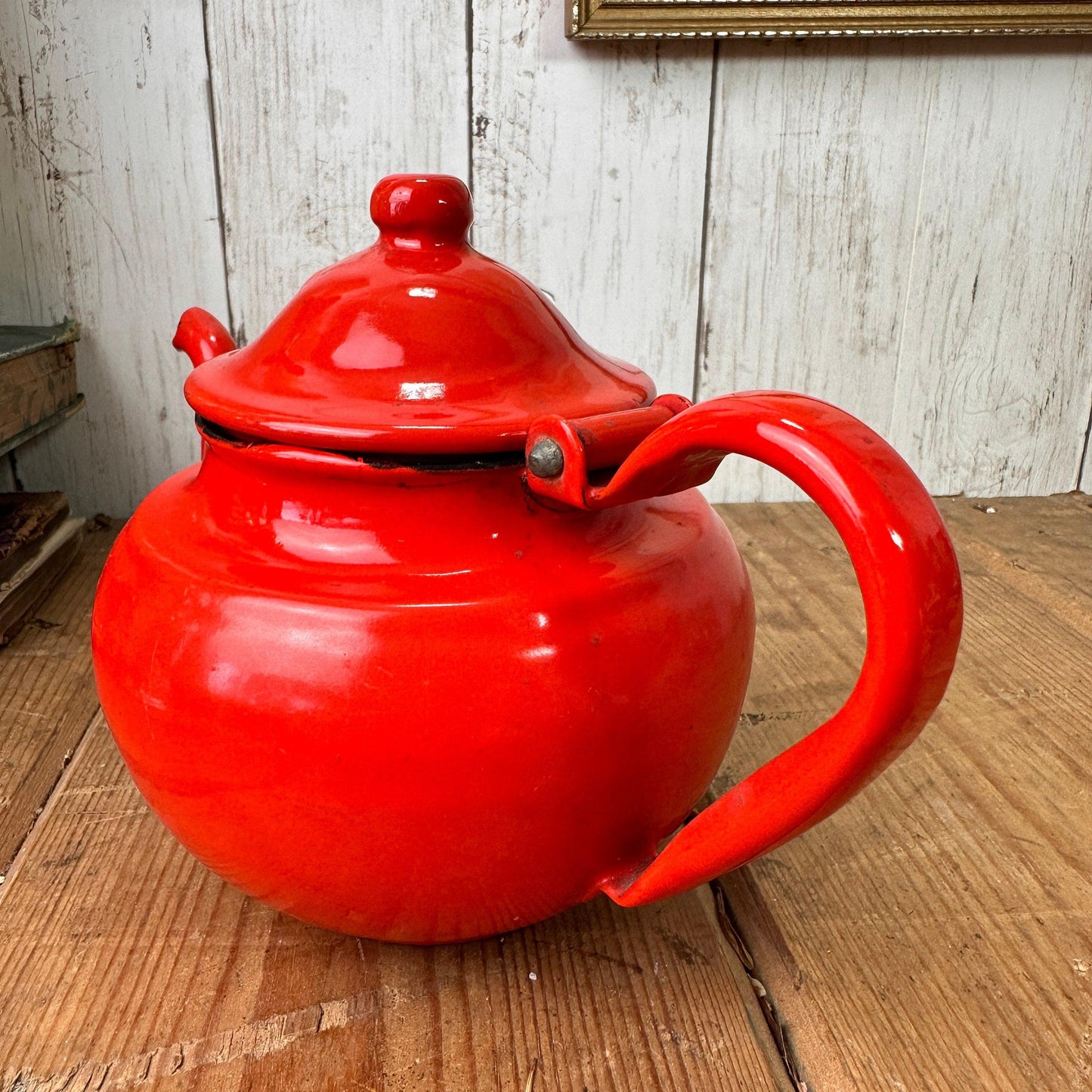 Bright red vintage enamel teapot with lid on wooden surface against white wood wall