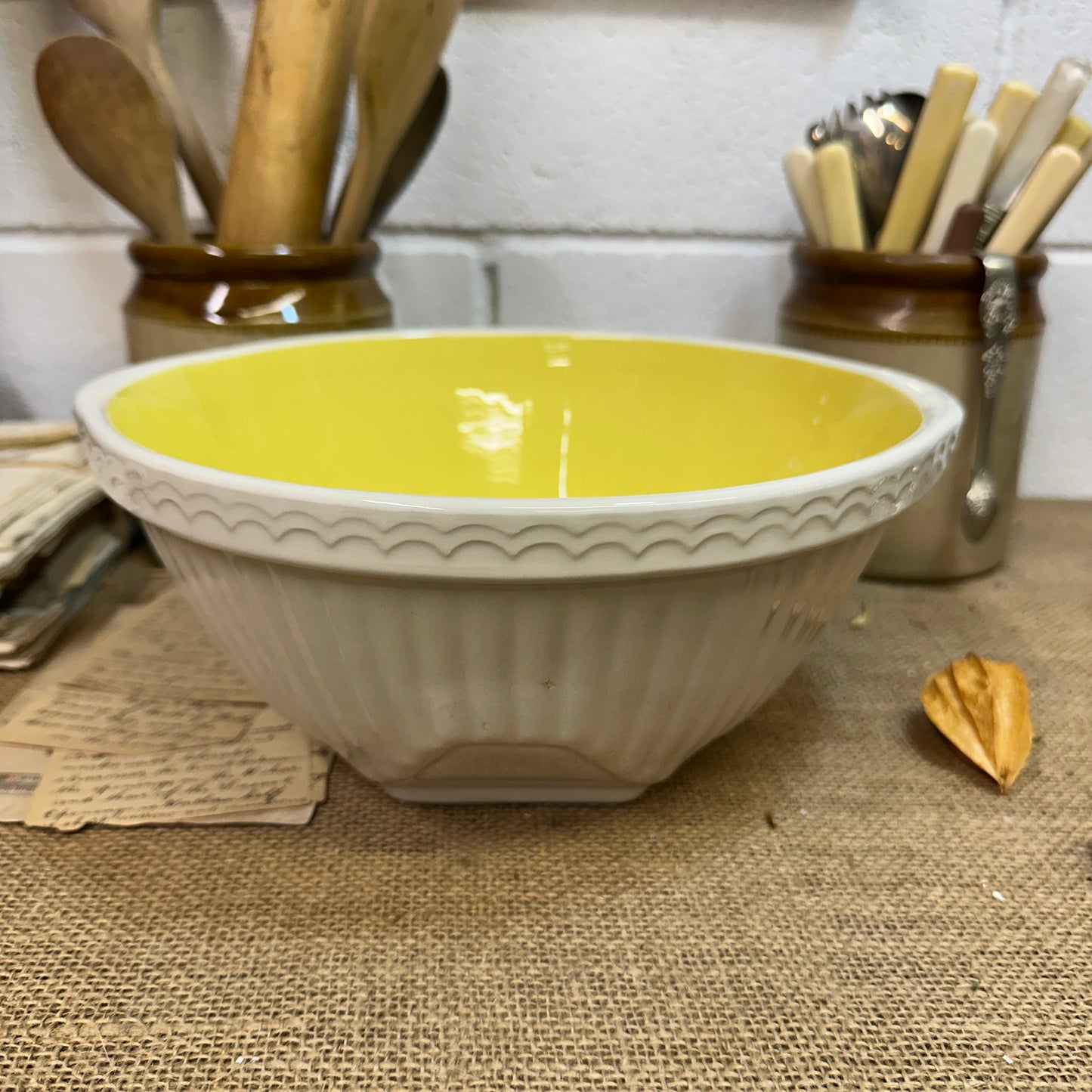 Vintage ceramic mixing bowl with yellow interior on burlap tablecloth in rustic kitchen