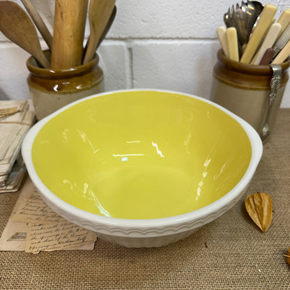 Ceramic mixing bowl with yellow interior and white exterior on rustic table with wooden utensils