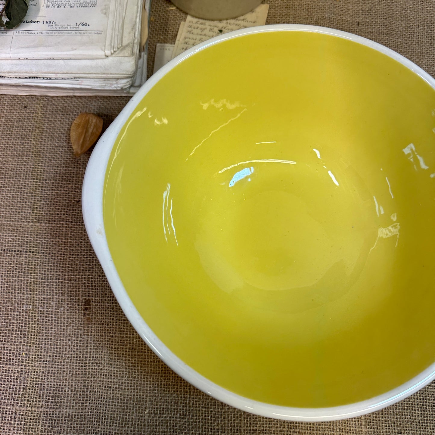 Empty ceramic mixing bowl with yellow interior and white exterior on burlap cloth with vintage papers