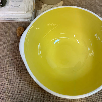 Empty ceramic mixing bowl with yellow interior and white exterior on burlap cloth with vintage papers