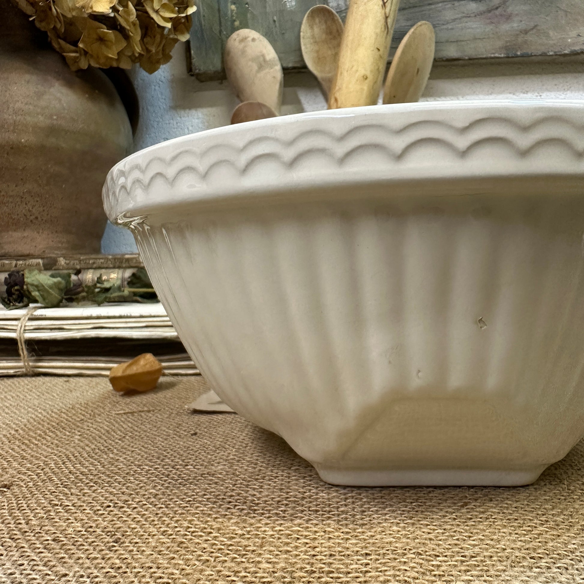 White ceramic bowl with scalloped edge and wooden spoons inside on rustic woven cloth