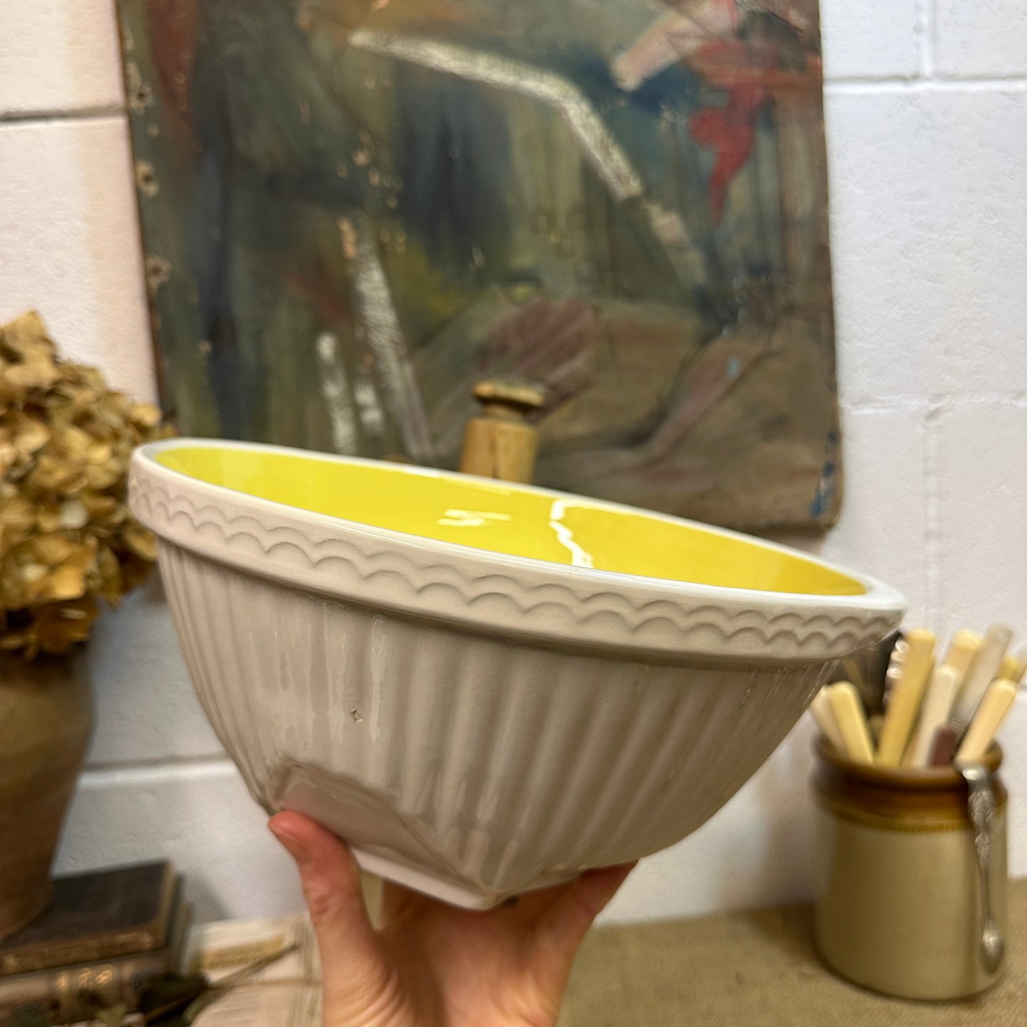 Hand holding a beige ceramic bowl with yellow glossy interior and decorative edge in a rustic kitchen setting