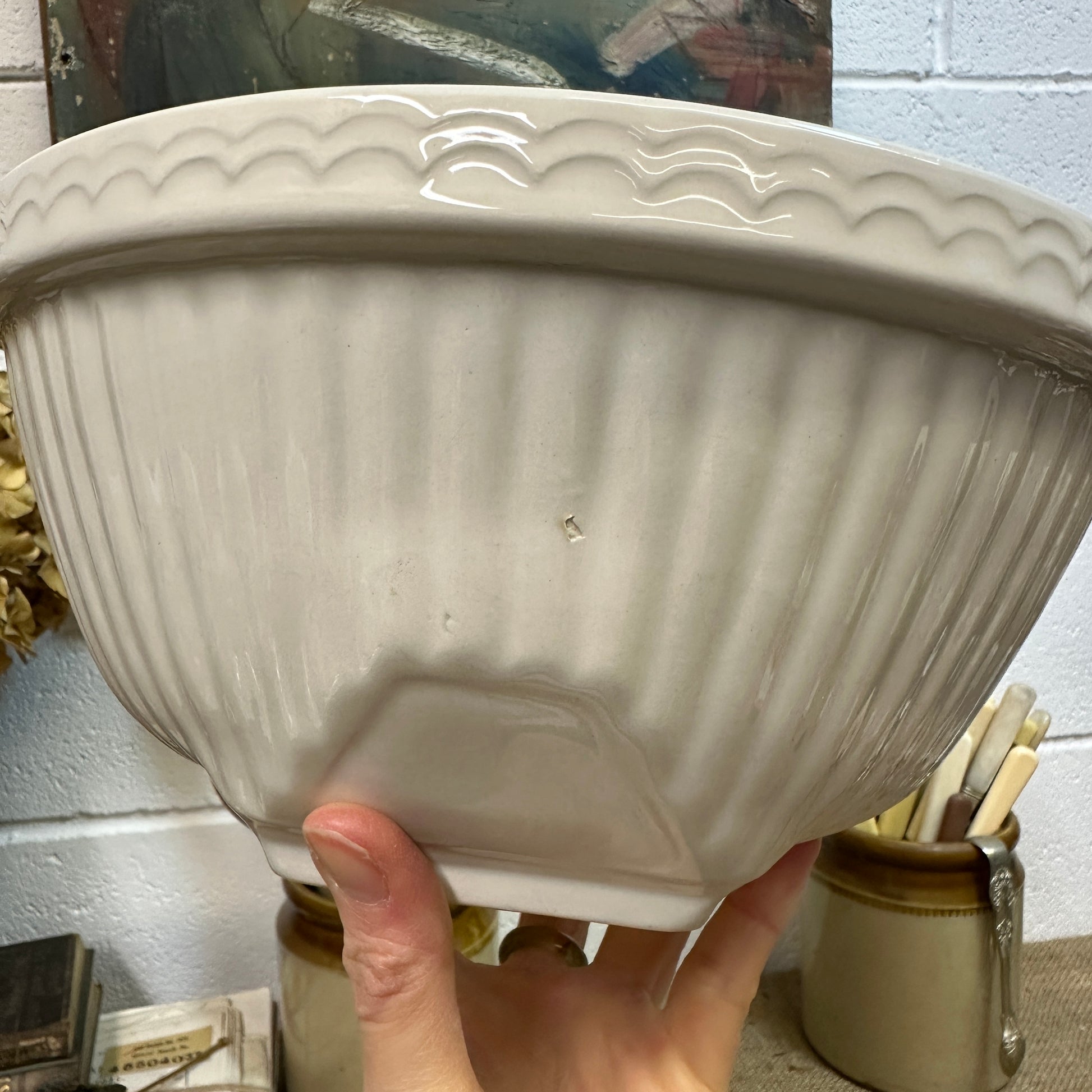 Hand holding vintage white ceramic bowl with fluted sides and decorative rim in rustic kitchen setting