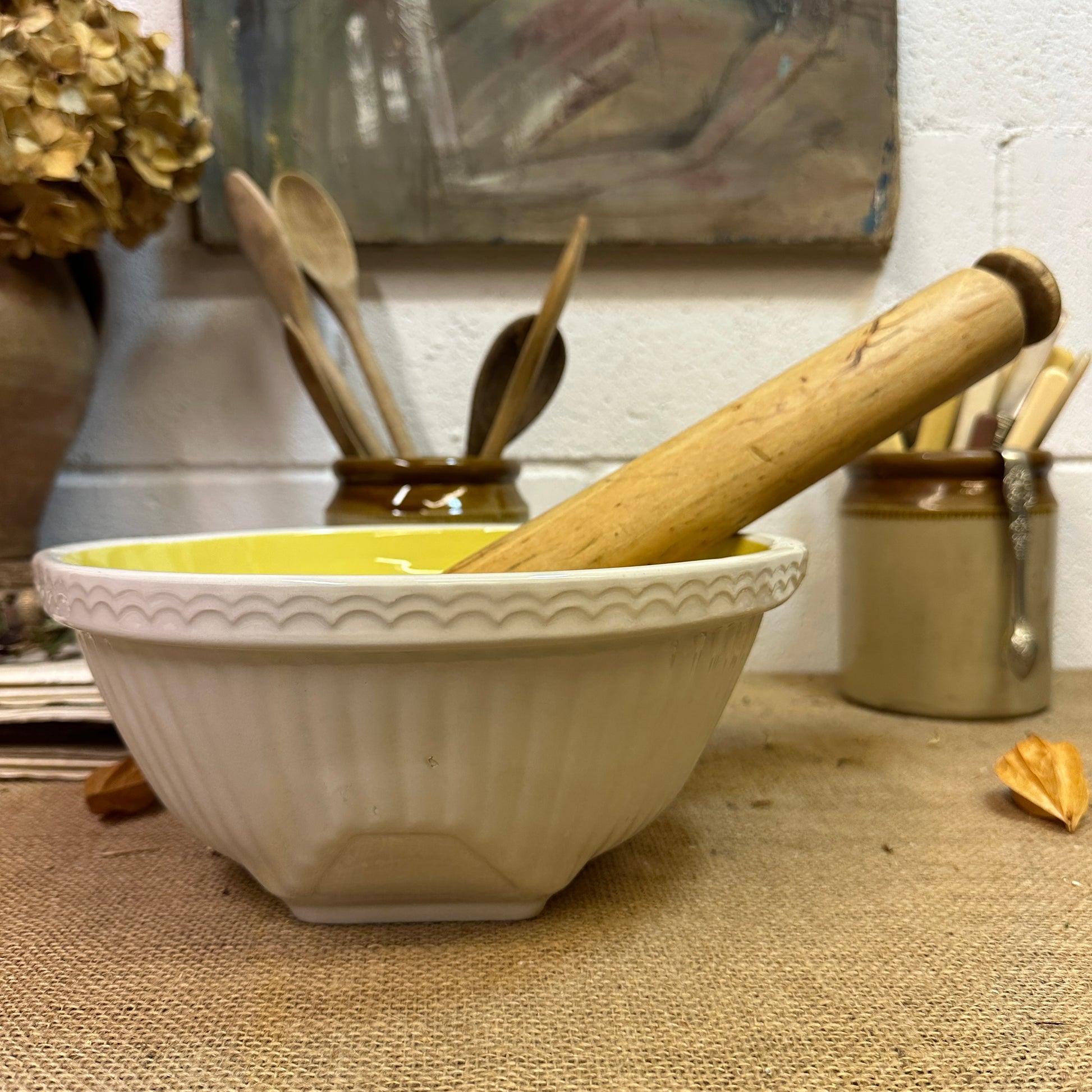 White ceramic mixing bowl with yellow interior and wooden rolling pin on burlap cloth